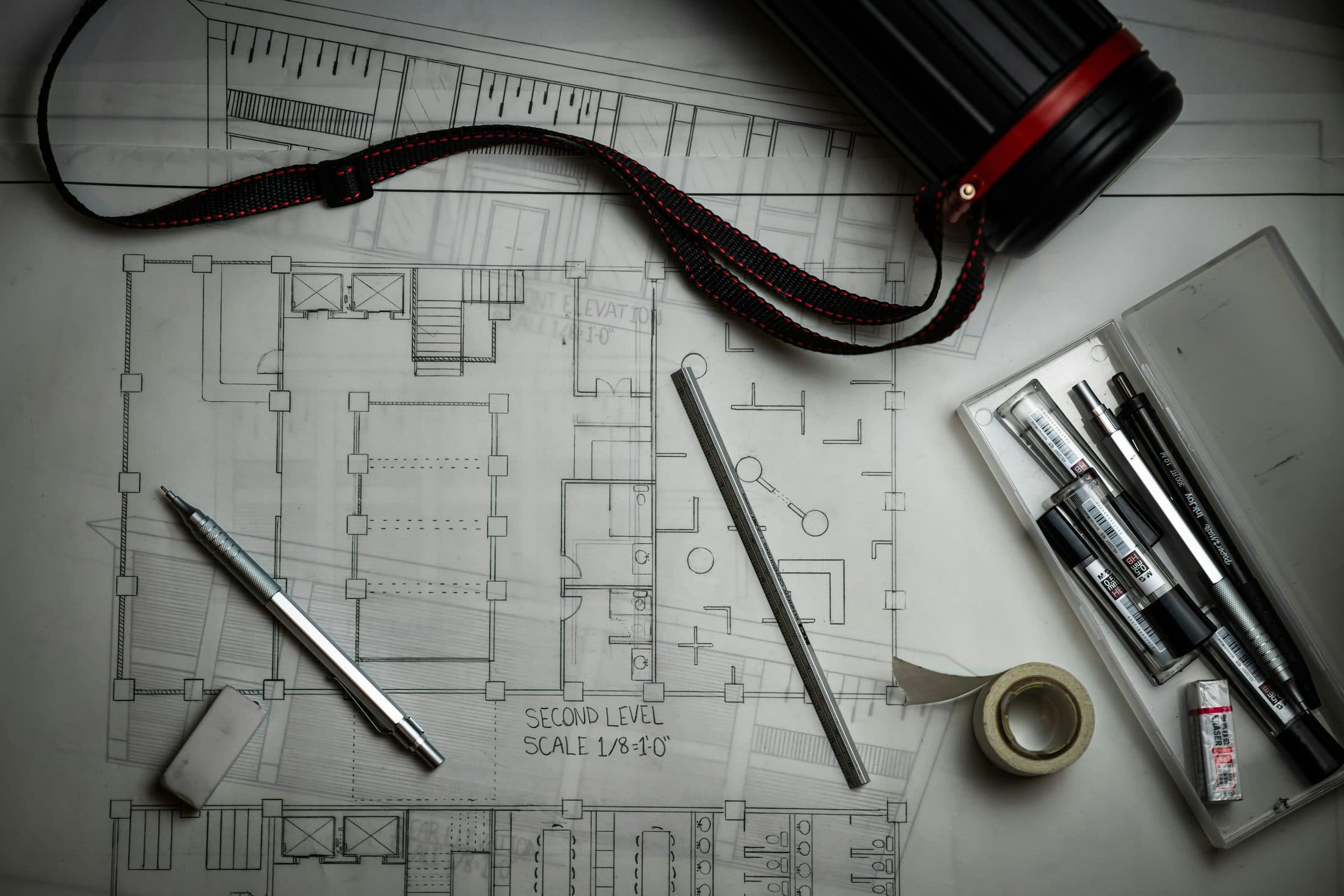 Un plan d'étage étalé sur une table, avec stylos techniques, règle métallique et tube porte-plans